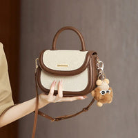 Stylish beige and brown leather handbag with top handle and cute plush keychain accessory