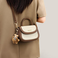 Woman with a beige dress carrying a small brown and cream crossbody handbag with a plush keychain
