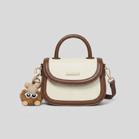 Cream and brown leather handbag with handle, crossbody strap, and bear keychain accessory