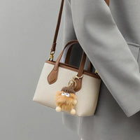 Beige and brown leather handbag with cute fluffy keychain, worn over a grey coat