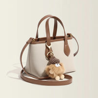 Beige leather handbag with brown trim and cute fluffy pompom keychain