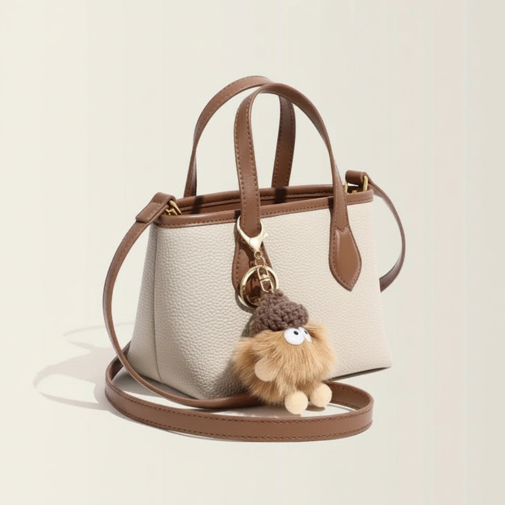 Beige leather handbag with brown trim and cute fluffy pompom keychain