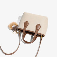 Beige and brown leather crossbody bag with plush keychain on white background