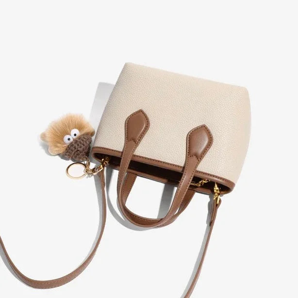 Beige and brown leather crossbody bag with plush keychain on white background