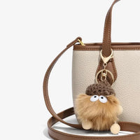 Beige crossbody handbag with brown trim and a fluffy acorn keychain accessory