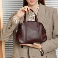 Woman in tan blazer holding a small brown leather handbag in front of blinds