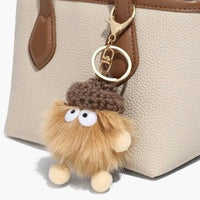 Cute fuzzy acorn keychain with googly eyes on beige leather handbag