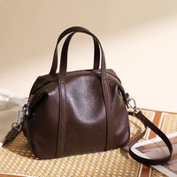 Dark brown leather handbag with top handles and shoulder strap on woven mat
