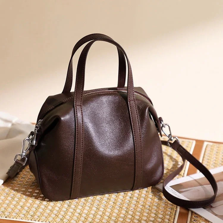 Dark brown leather handbag with top handles and shoulder strap on woven mat