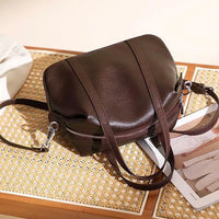 Dark brown leather crossbody bag on woven table with magazine and soft lighting