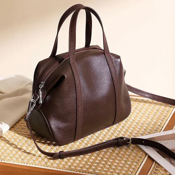 Dark brown leather handbag with top handles and strap on a woven mat