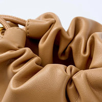 Close-up of tan ruched leather handbag with gold hardware on white background