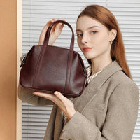 Woman in blazer holding a brown leather handbag in front of blinds