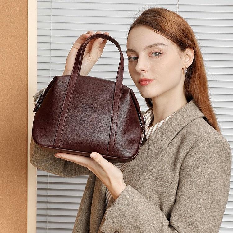 Woman in blazer holding a brown leather handbag in front of blinds