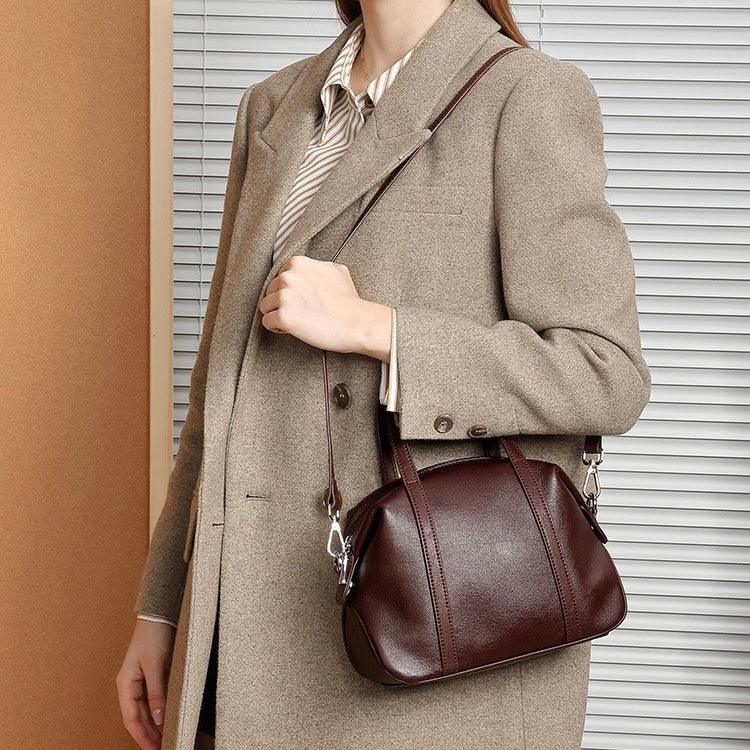 Woman in beige blazer holding a brown leather handbag with shoulder strap indoors