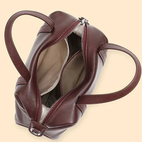 Open burgundy leather handbag with double handles and beige fabric lining