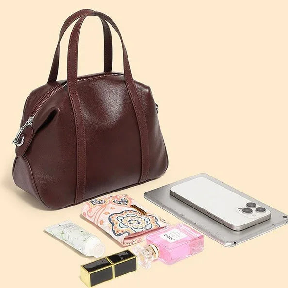 Brown leather handbag with phone, cosmetics, wallet, perfume, and tablet on beige background