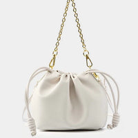 White drawstring bucket bag with gold chain strap on plain background