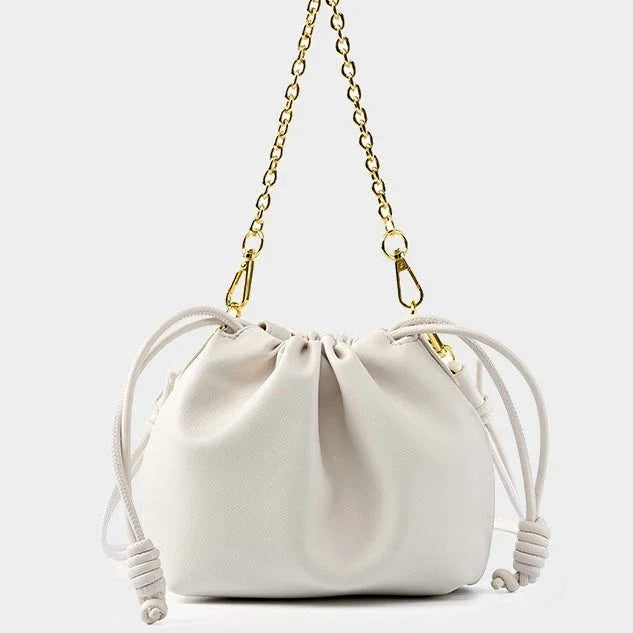 White drawstring bucket bag with gold chain strap on plain background
