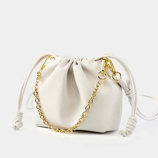 White drawstring pouch bag with gold chain strap on plain background