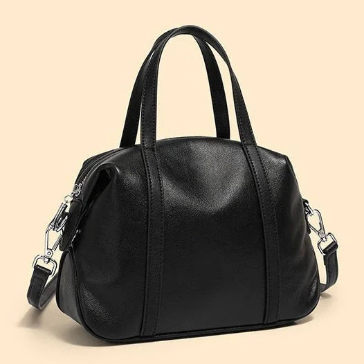 Black leather handbag with top handles and detachable shoulder strap on beige background