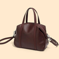 Brown leather handbag with dual handles and detachable shoulder strap on beige background