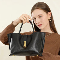 Woman in brown sweater holding black leather handbag with gold hardware