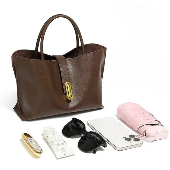 Brown leather tote bag with pink umbrella, sunglasses, smartphone, lipstick, and hand cream