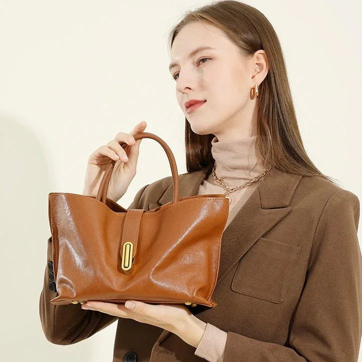 Woman in brown blazer holding a stylish brown leather handbag with gold buckle