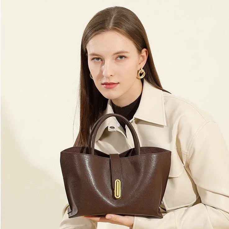 Woman in cream jacket holding elegant brown leather handbag with gold clasp