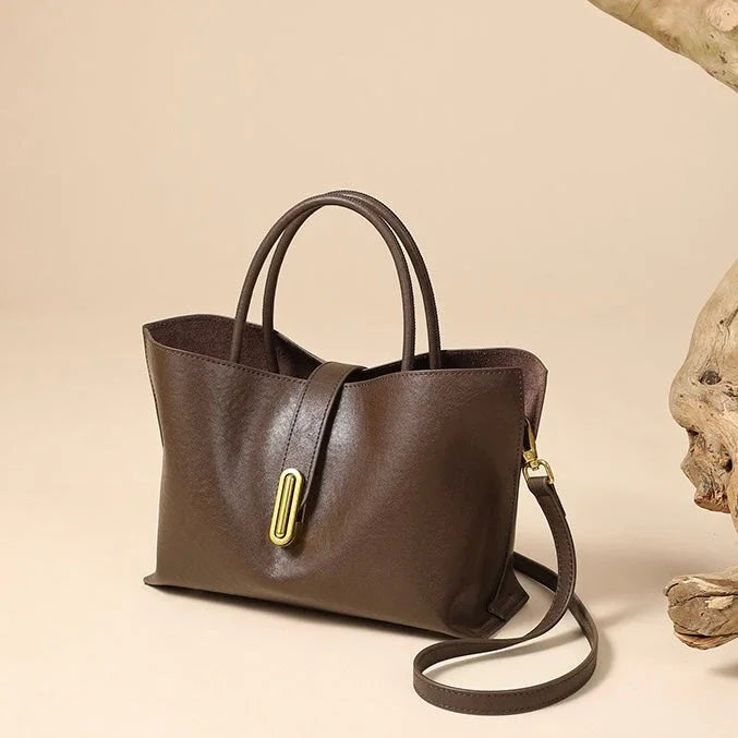 Brown leather handbag with gold hardware and detachable strap on beige background