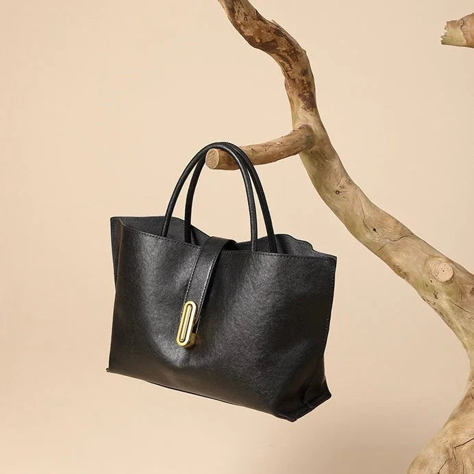 Black leather tote bag with gold accent on a wooden branch, beige background