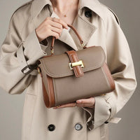 Woman in beige trench coat holding taupe leather handbag with gold buckle