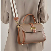 Taupe leather handbag with gold hardware and striped shoulder strap on beige blazer