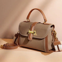 Taupe leather handbag with brown trim, gold clasp, and detachable strap on beige background