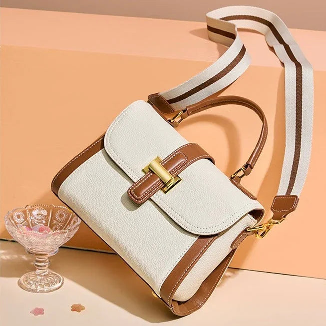White and brown leather crossbody handbag with gold clasp on peach background