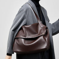 Woman in gray coat carrying large brown leather tote bag over shoulder