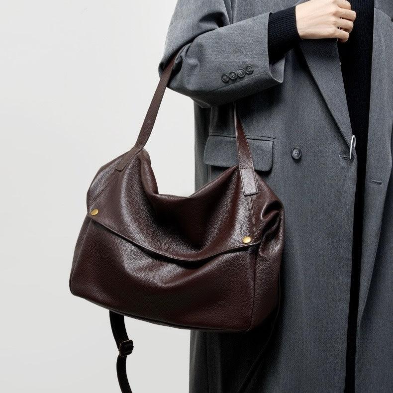 Woman in gray coat holding large brown leather shoulder bag with gold buttons