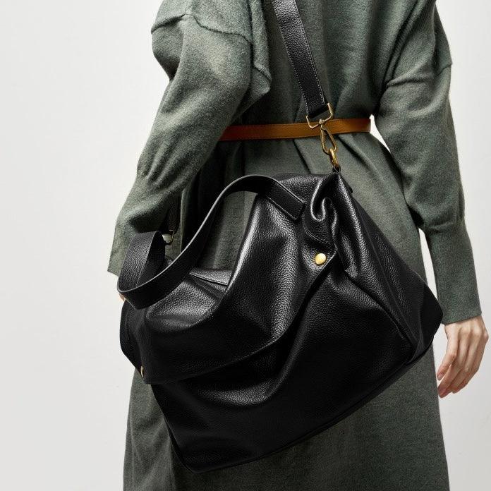 Woman in green dress with brown belt carrying large black leather shoulder bag