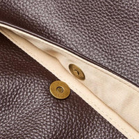 Close-up of brown leather bag with beige fabric lining and brass snap button closure