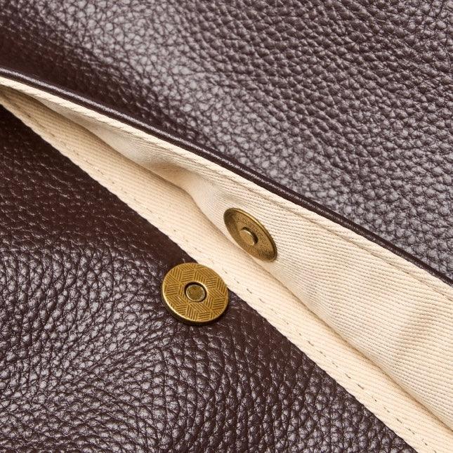 Close-up of brown leather bag with beige fabric lining and brass snap button closure