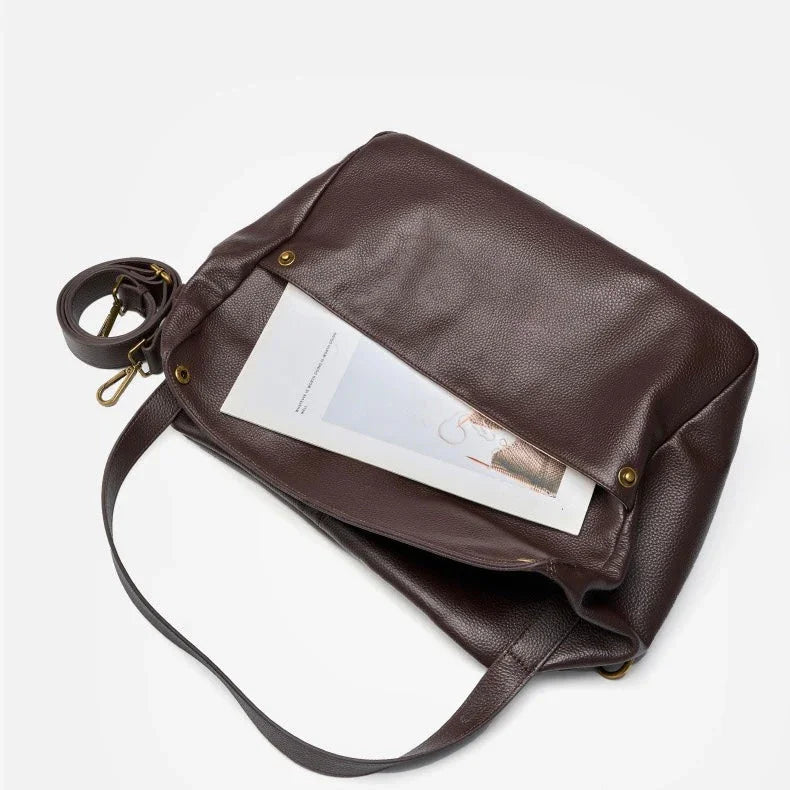 Brown leather messenger bag with magazine in front pocket on white background