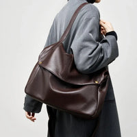 Woman in grey coat carrying large brown leather shoulder bag