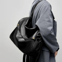 Person wearing gray coat carrying large black leather shoulder bag with gold studs