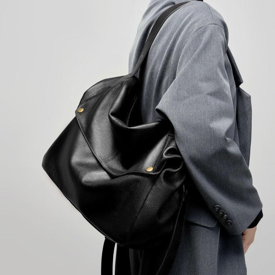 Person wearing gray coat carrying large black leather shoulder bag with gold studs