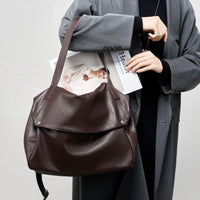 Woman in grey coat holding large brown leather shoulder bag and fashion magazine