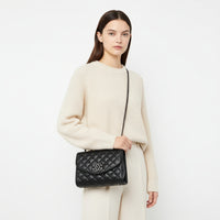 Black quilted leather shoulder bag with chain strap and metal logo, worn over white shirt