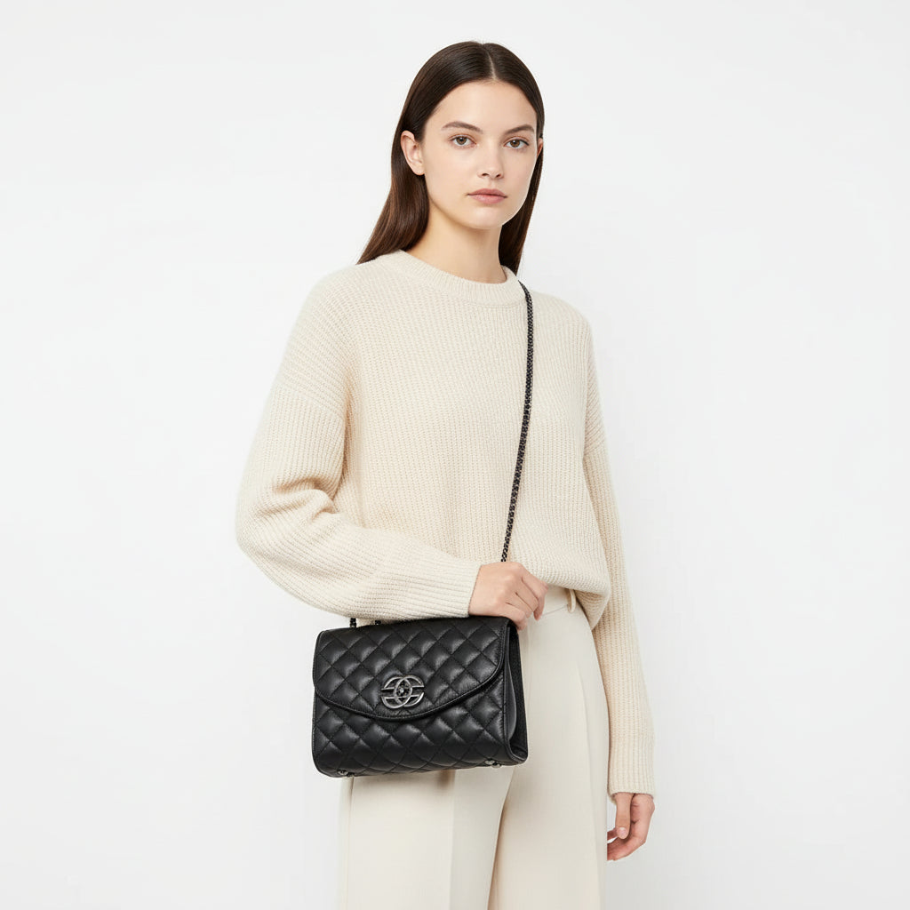 Black quilted leather shoulder bag with chain strap and metal logo, worn over white shirt