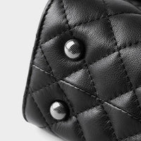 Close-up of quilted black leather bag with silver stud details on a light background