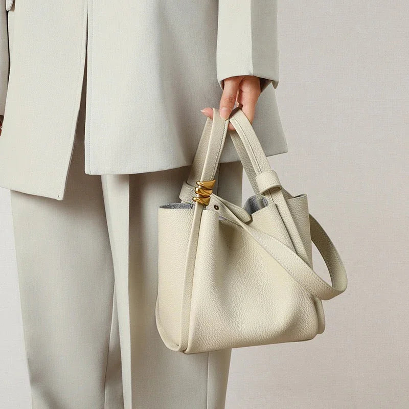 Woman in a cream suit holding a minimalist beige leather handbag